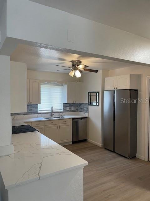 kitchen featuring backsplash, appliances with stainless steel finishes, light wood-style floors, and a sink