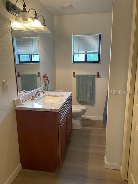 bathroom with visible vents, toilet, wood finished floors, baseboards, and vanity