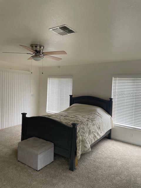 carpeted bedroom with visible vents, a textured ceiling, and a ceiling fan