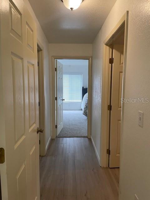 corridor with light wood finished floors, baseboards, and a textured wall