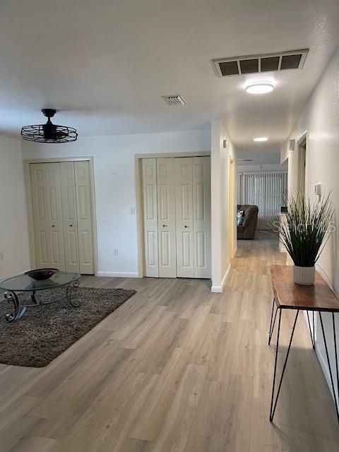 hall featuring light wood-style flooring, baseboards, and visible vents