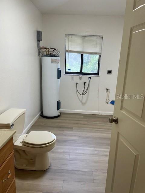 bathroom featuring baseboards, toilet, water heater, wood finished floors, and vanity