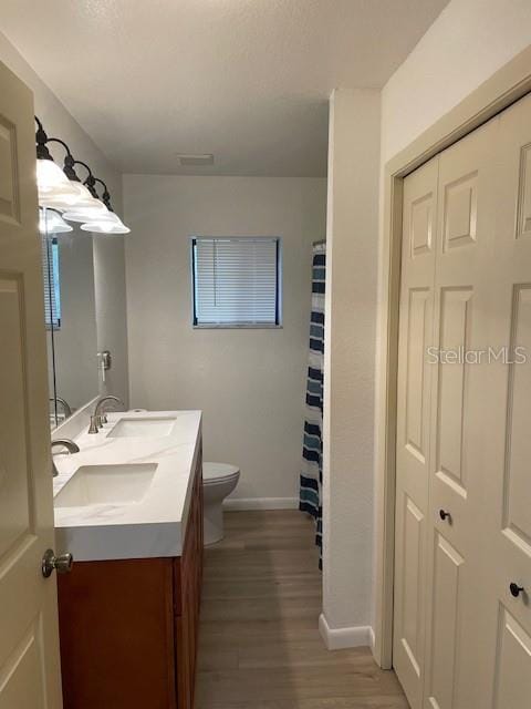 bathroom with double vanity, toilet, wood finished floors, and a sink