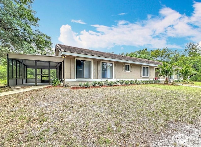 ranch-style house featuring an attached carport, stucco siding, a sunroom, and a front yard