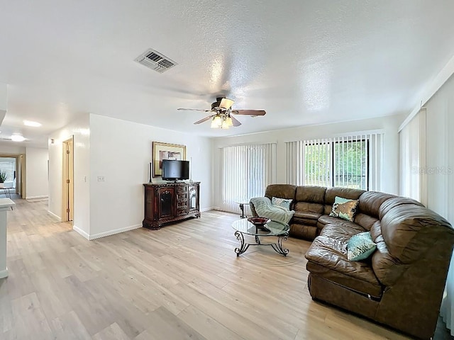 living area with baseboards, a textured ceiling, light wood finished floors, visible vents, and a ceiling fan