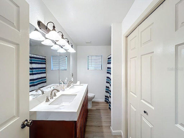 full bathroom with double vanity, a sink, toilet, and wood finished floors