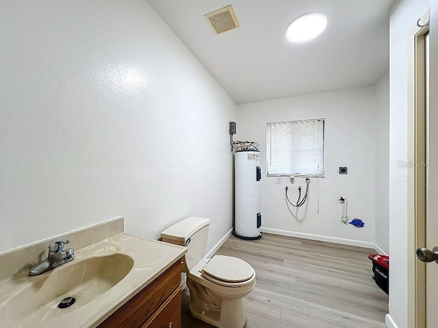 bathroom with toilet, vanity, wood finished floors, electric water heater, and visible vents