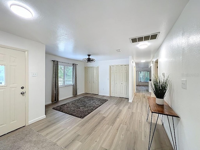 foyer featuring baseboards, light wood-style floors, a chandelier, and visible vents