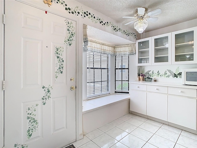 interior space with a textured ceiling, white cabinetry, light countertops, glass insert cabinets, and white microwave