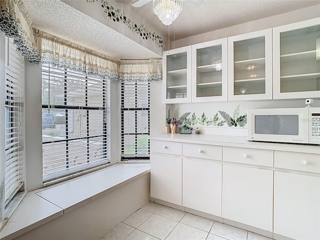 interior space featuring a textured ceiling, light tile patterned flooring, light countertops, glass insert cabinets, and white microwave