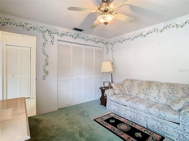 carpeted living room with visible vents, a textured ceiling, and a ceiling fan