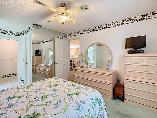 bedroom featuring ensuite bath, visible vents, a textured ceiling, and a ceiling fan