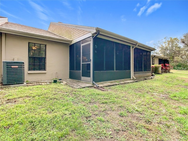 rear view of property featuring central AC unit, a lawn, a sunroom, and stucco siding