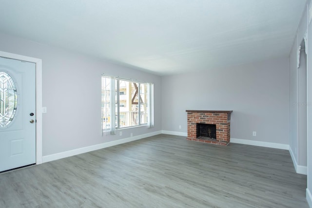 unfurnished living room featuring baseboards, a brick fireplace, and wood finished floors