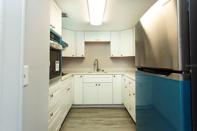 kitchen featuring visible vents, freestanding refrigerator, light wood-style floors, white cabinets, and a sink