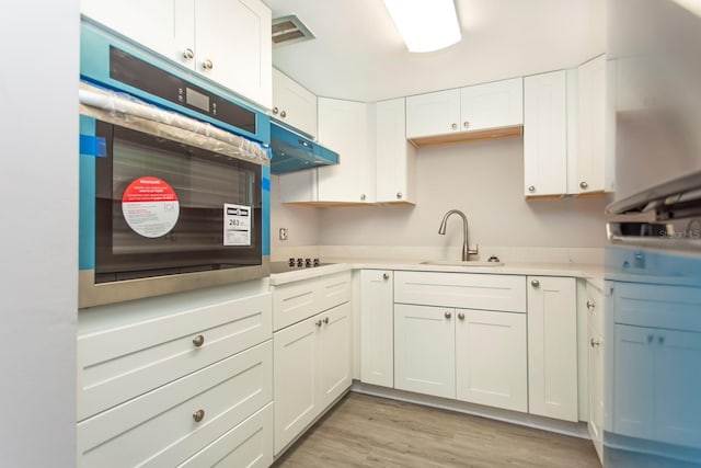 kitchen with under cabinet range hood, stainless steel oven, white cabinets, black electric cooktop, and a sink