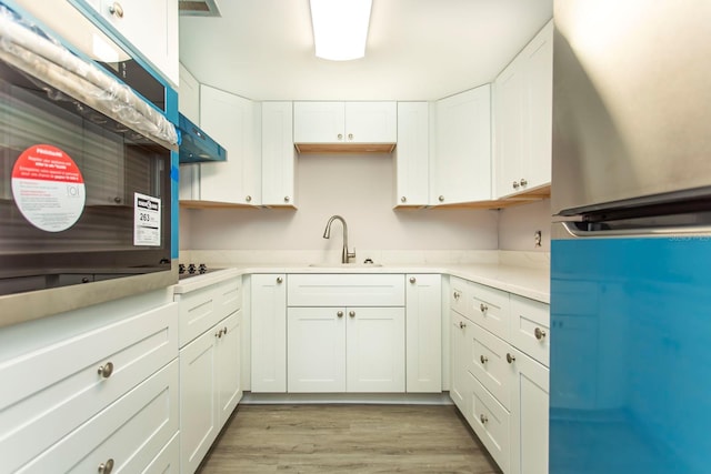 kitchen with white cabinetry, fridge, light wood-style flooring, and a sink