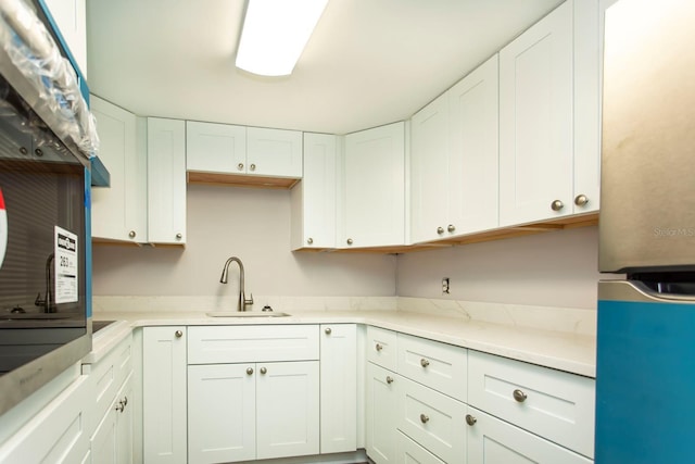 kitchen featuring freestanding refrigerator, white cabinets, light countertops, and a sink