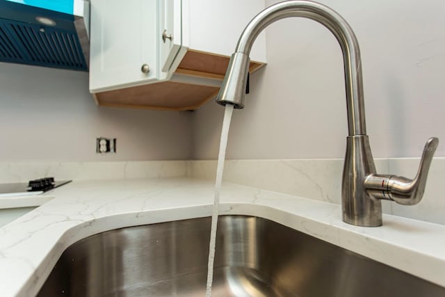 room details with a sink, light stone countertops, extractor fan, and white cabinets