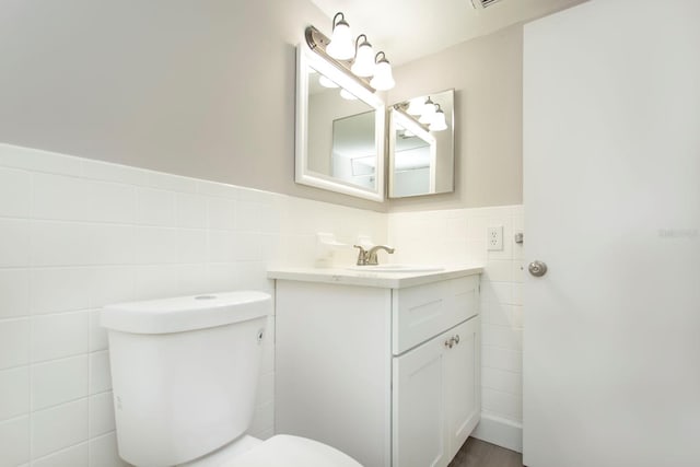 half bathroom with a wainscoted wall, vanity, toilet, and tile walls