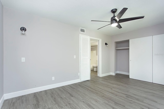 unfurnished bedroom featuring connected bathroom, visible vents, baseboards, and wood finished floors