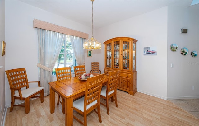 dining space featuring light wood-style flooring, a notable chandelier, and baseboards