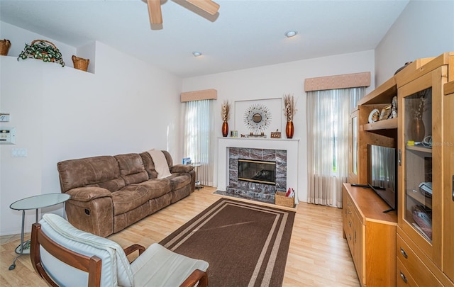 living room with light wood-style floors, ceiling fan, and a tiled fireplace