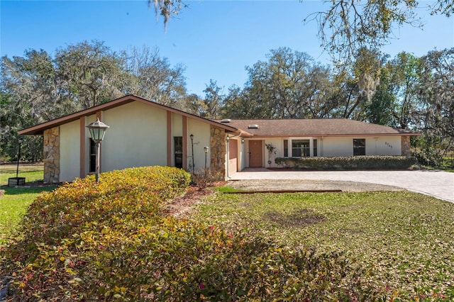 ranch-style home with stucco siding, a front yard, a garage, and driveway