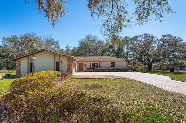 ranch-style house featuring a front lawn, decorative driveway, and stucco siding