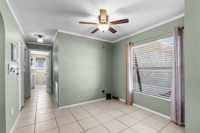 spare room featuring a ceiling fan, a textured ceiling, light tile patterned flooring, crown molding, and baseboards