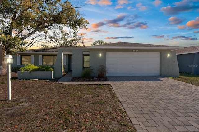 ranch-style house featuring stucco siding, an attached garage, and decorative driveway