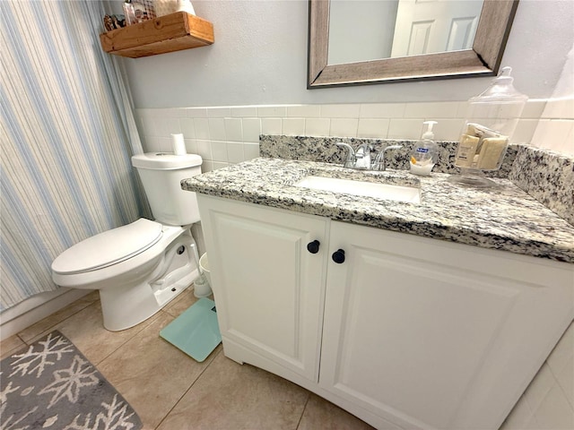 bathroom with vanity, wainscoting, tile patterned floors, toilet, and tile walls