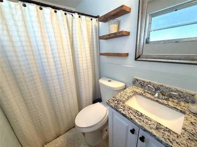 bathroom featuring vanity, tile walls, toilet, and a wainscoted wall