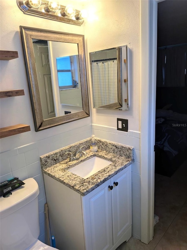 bathroom featuring a wainscoted wall, toilet, tile walls, and vanity