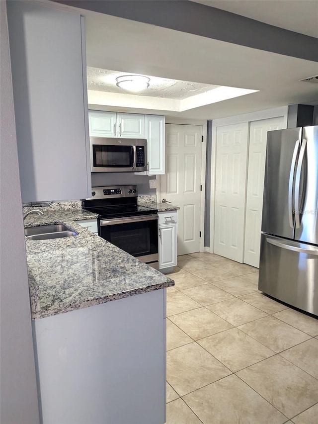 kitchen featuring light stone counters, light tile patterned floors, a sink, stainless steel appliances, and white cabinetry