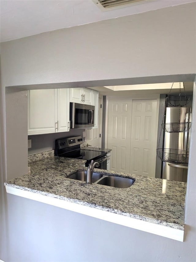 kitchen featuring a sink, stainless steel appliances, light stone counters, and white cabinetry