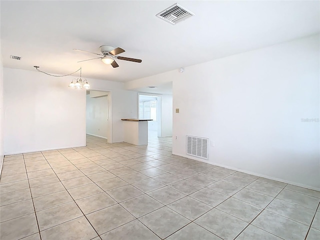 spare room featuring light tile patterned flooring, visible vents, and ceiling fan with notable chandelier