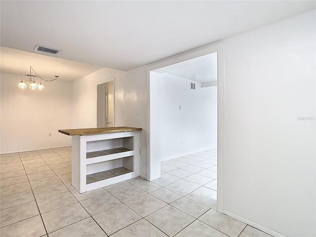 empty room with light tile patterned flooring, visible vents, and an inviting chandelier