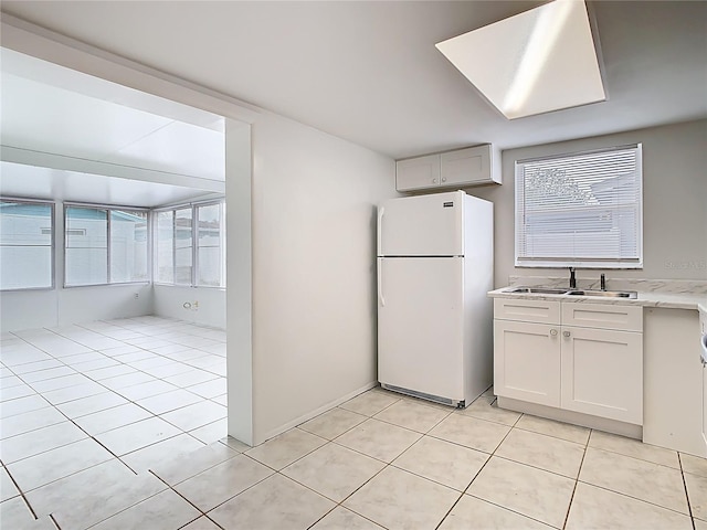 kitchen featuring light tile patterned floors, freestanding refrigerator, a sink, light countertops, and white cabinets