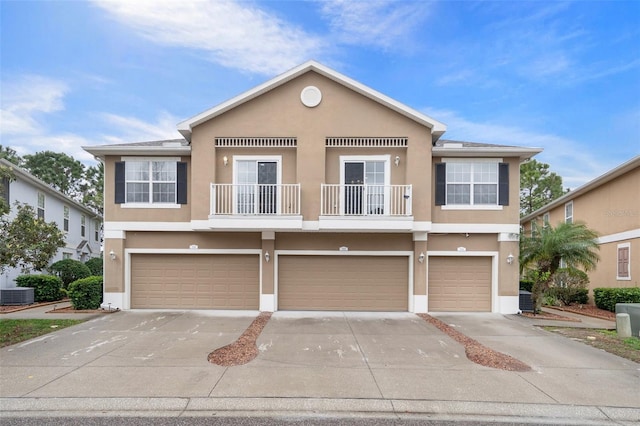 view of property featuring central air condition unit, stucco siding, a balcony, a garage, and driveway