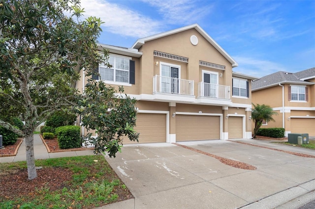 townhome / multi-family property featuring stucco siding, driveway, cooling unit, an attached garage, and a balcony