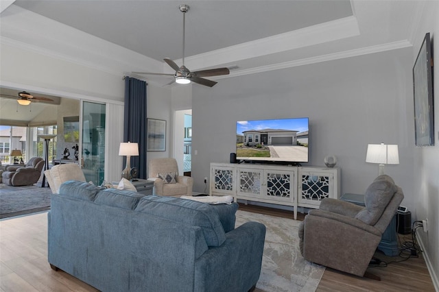 living area with baseboards, ceiling fan, a tray ceiling, ornamental molding, and wood finished floors