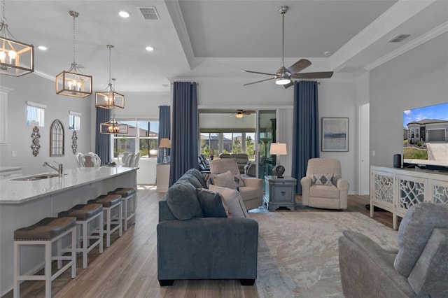 living room featuring light wood finished floors, visible vents, crown molding, and a tray ceiling