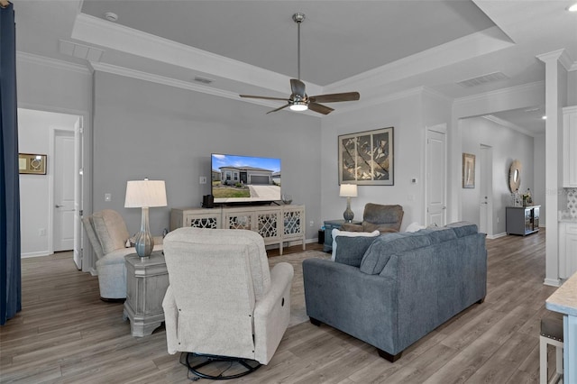 living area with a tray ceiling, light wood-style flooring, crown molding, and visible vents