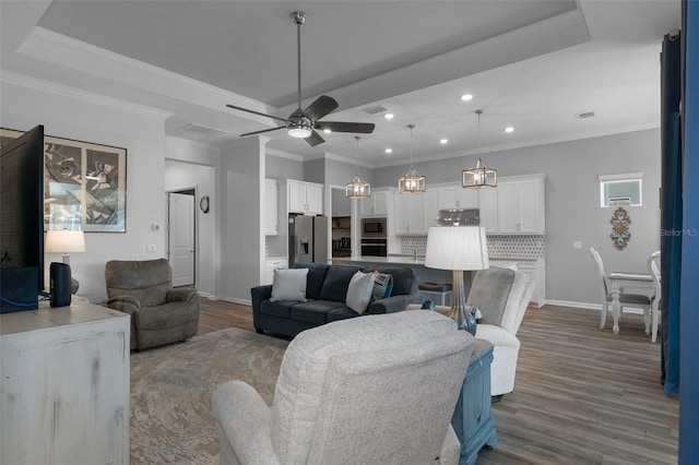 living room featuring wood finished floors, baseboards, a tray ceiling, ceiling fan, and crown molding