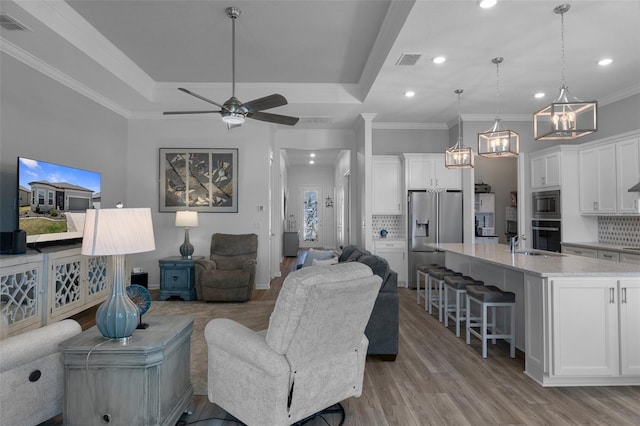 living area with a raised ceiling, ornamental molding, visible vents, and light wood-type flooring