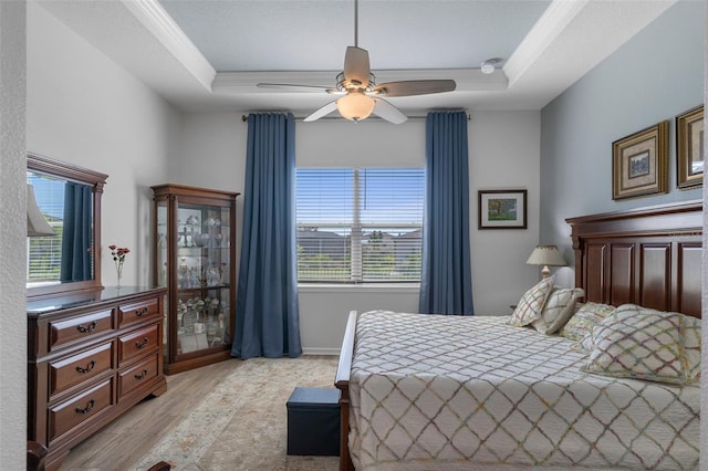 bedroom featuring ceiling fan, light wood-type flooring, a tray ceiling, and ornamental molding