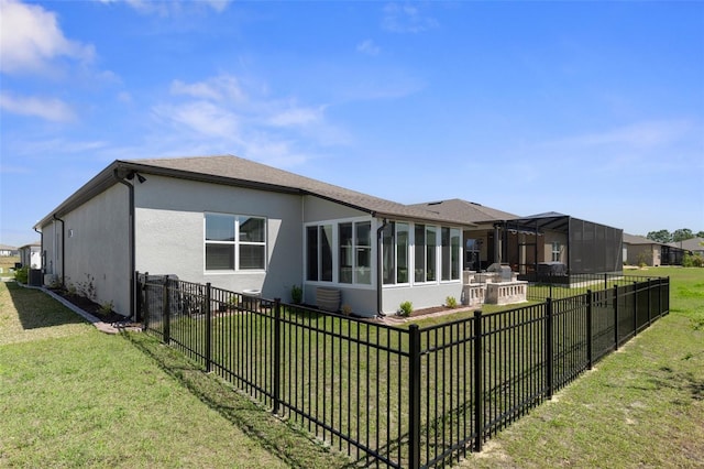 rear view of property with stucco siding, a lawn, a fenced backyard, and a sunroom