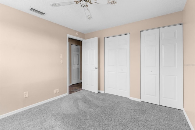 unfurnished bedroom featuring visible vents, baseboards, carpet, and multiple closets