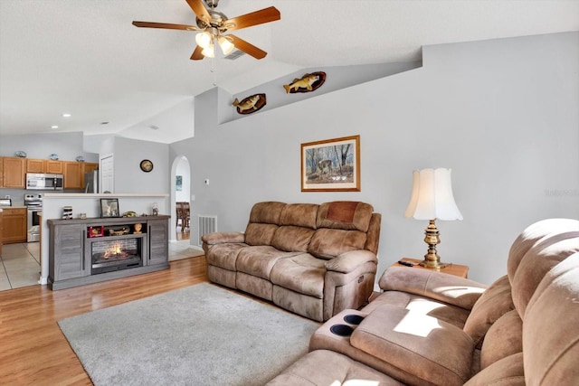 living area with arched walkways, visible vents, light wood finished floors, and vaulted ceiling